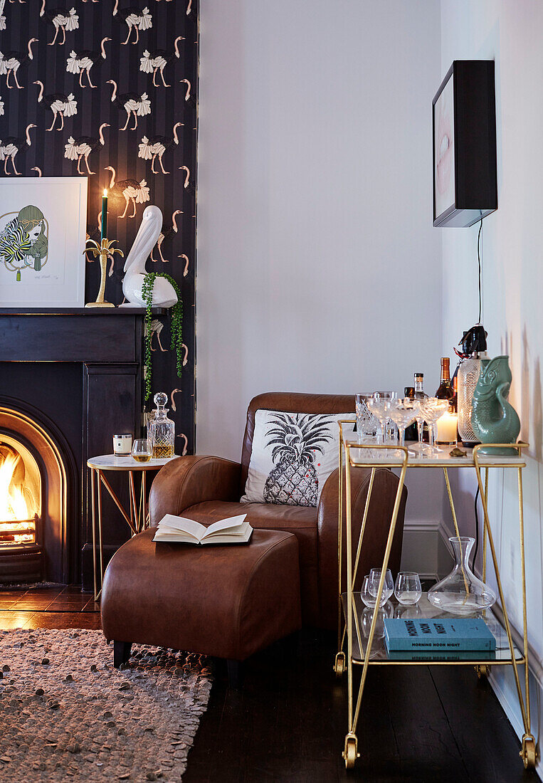 Brown leather armchair and footstool with dark wallpaper at fireside in Victorian semi-detached house South East London, UK