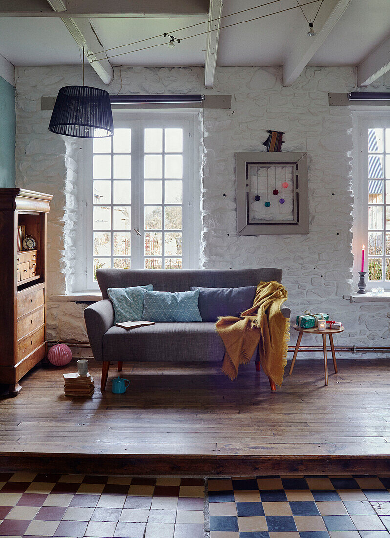 Graues Sofa auf Holzplattform in weiß getünchtem bretonischen Landhaus in Frankreich