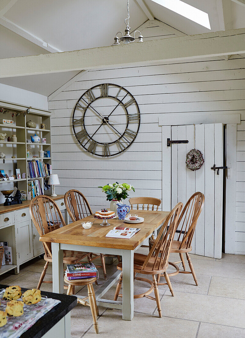 Esstisch und Stühle aus Holz mit großer Uhr in einem Bauernhaus in Northumberland, UK