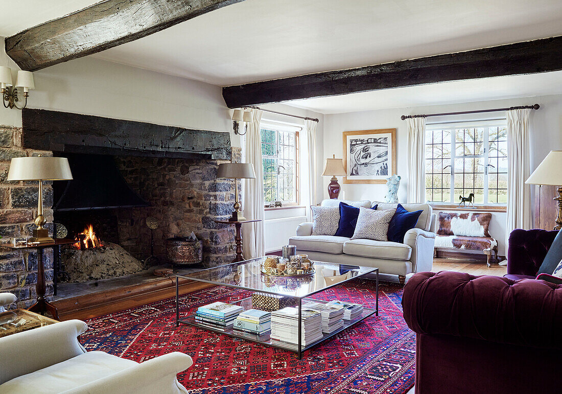 Glass coffee table and red patterned rug with lit fire in Devon living room, UK