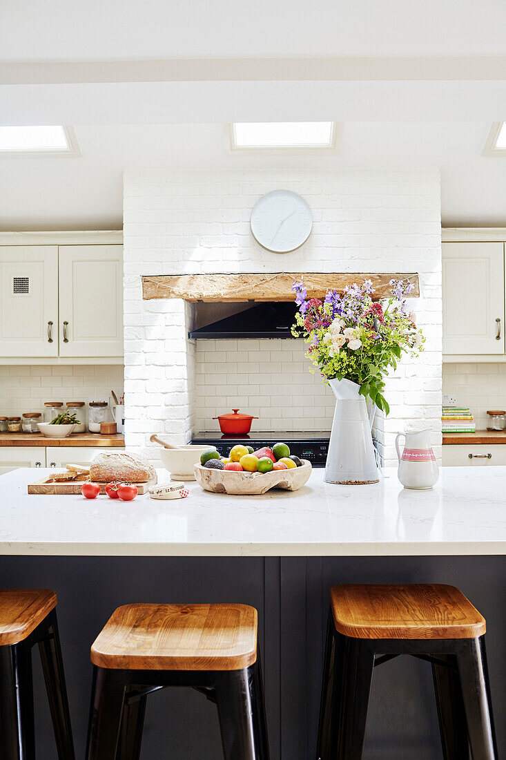 Cut flowers and fruit on worktop with bar stools in Oxfordshire kitchen, UK