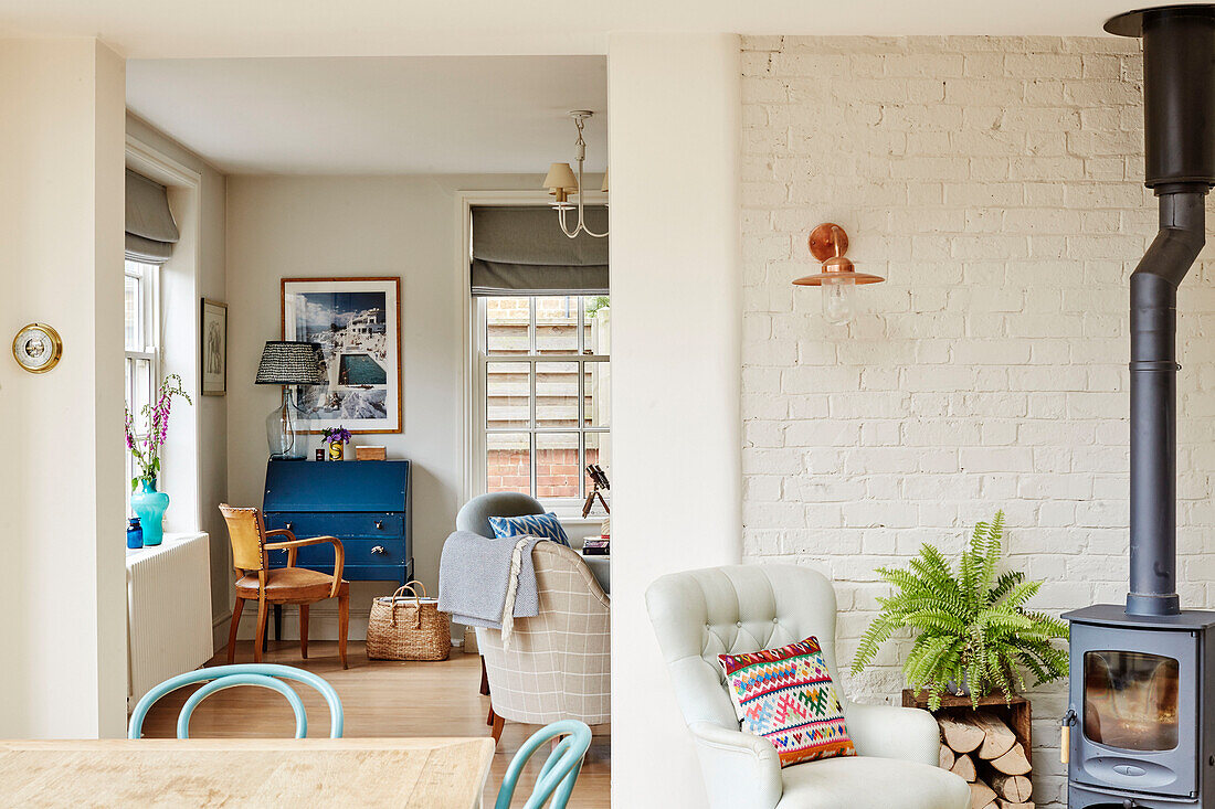 Buttoned armchair and fern beside woodburner with view of upcycled writing desk in Oxfordshire home, UK