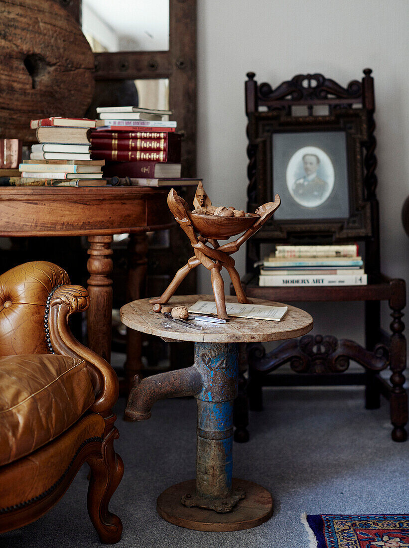 African bowl on side table made of salvaged pipe with books and chairs in North Yorkshire farmhouse, UK