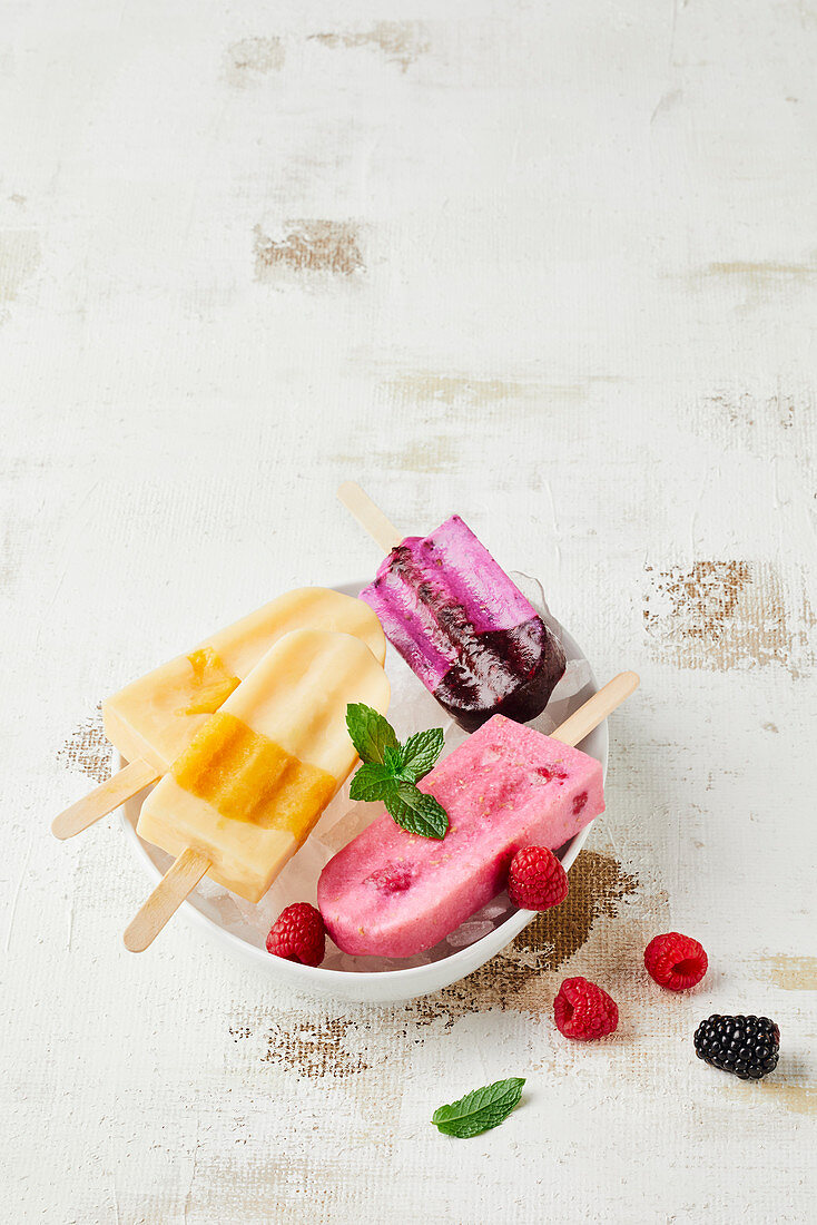 Various ice lollies (buttermilk, raspberry, blackberry, apricot) in a bowl of ice cubes