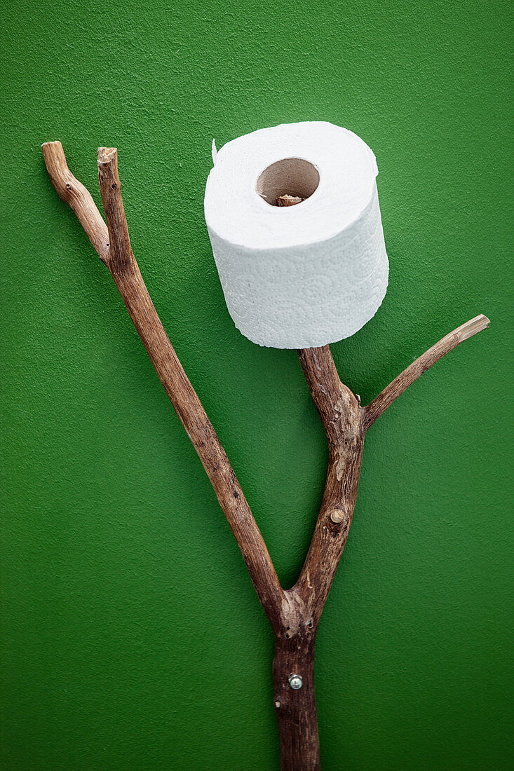 Ast als Toilettenrollenhalter an grüner Wand