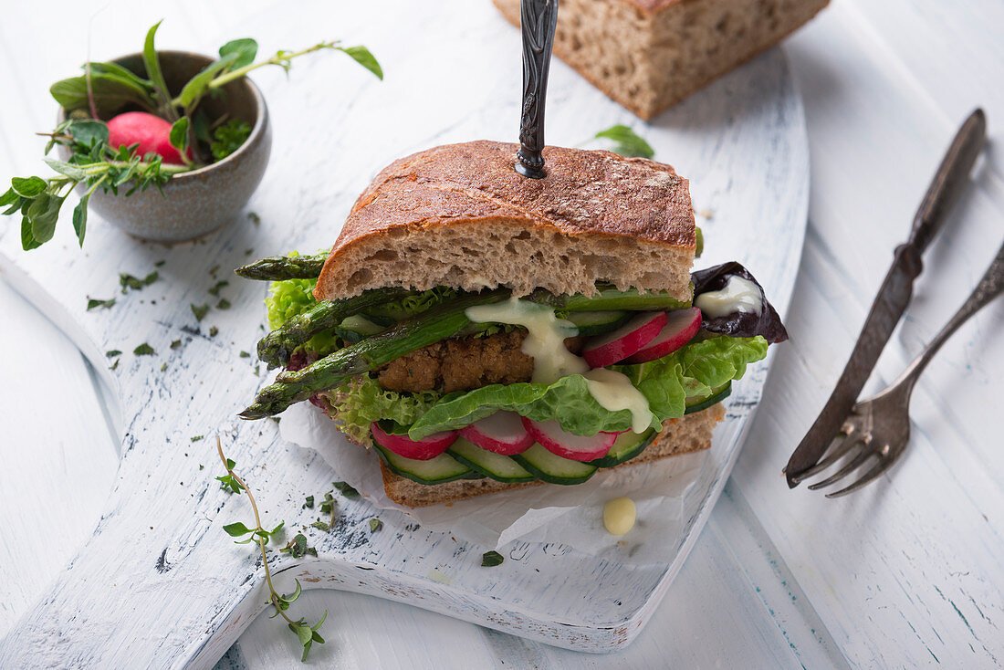 A sandwich with a bean patty, vegetables, lettuce, grilled asparagus and vegan Hollandaise