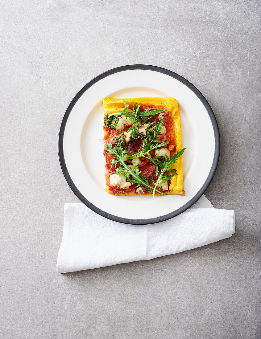 A slice of vegan polenta pizza with tomatoes, onions and pesto