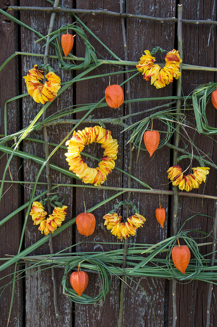 Wall hanging with roses and Chinese reed: Wreath made of petals and Chinese reed, lampion fruit as decoration