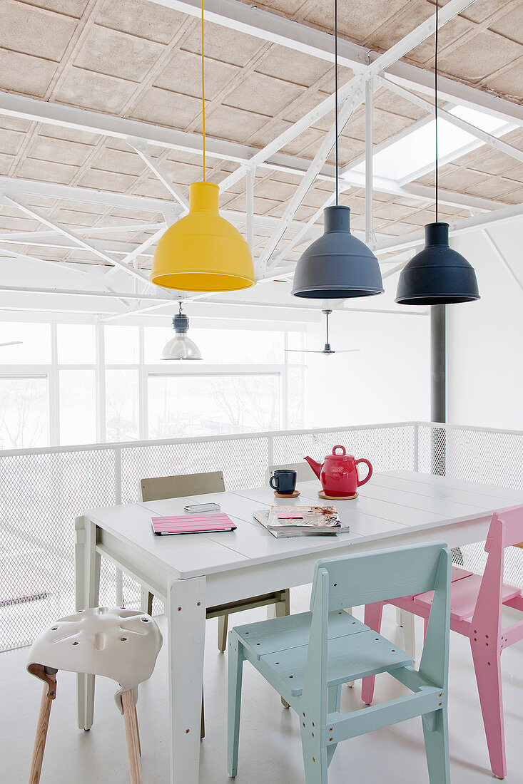 Industrial lamps above dining table and colourful chairs in loft apartment