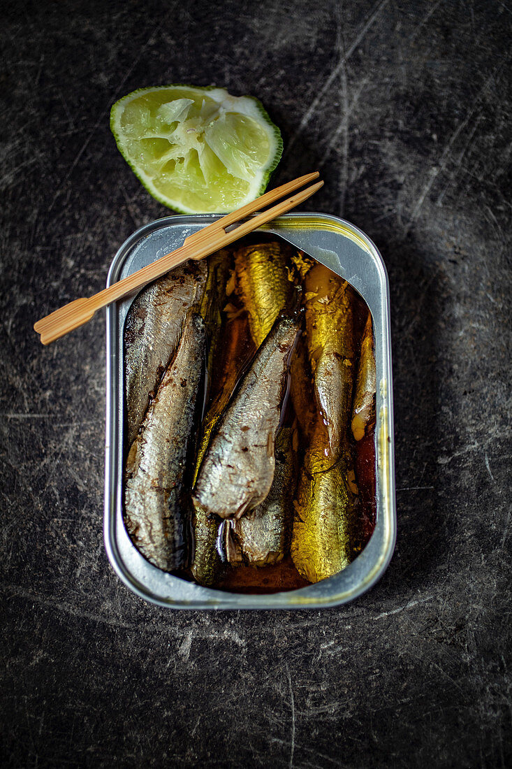 Sardines in a tin with a wooden fork and lime