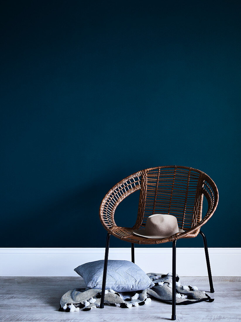 Hat on woven easy hair with cushions and blanket below against blue wall