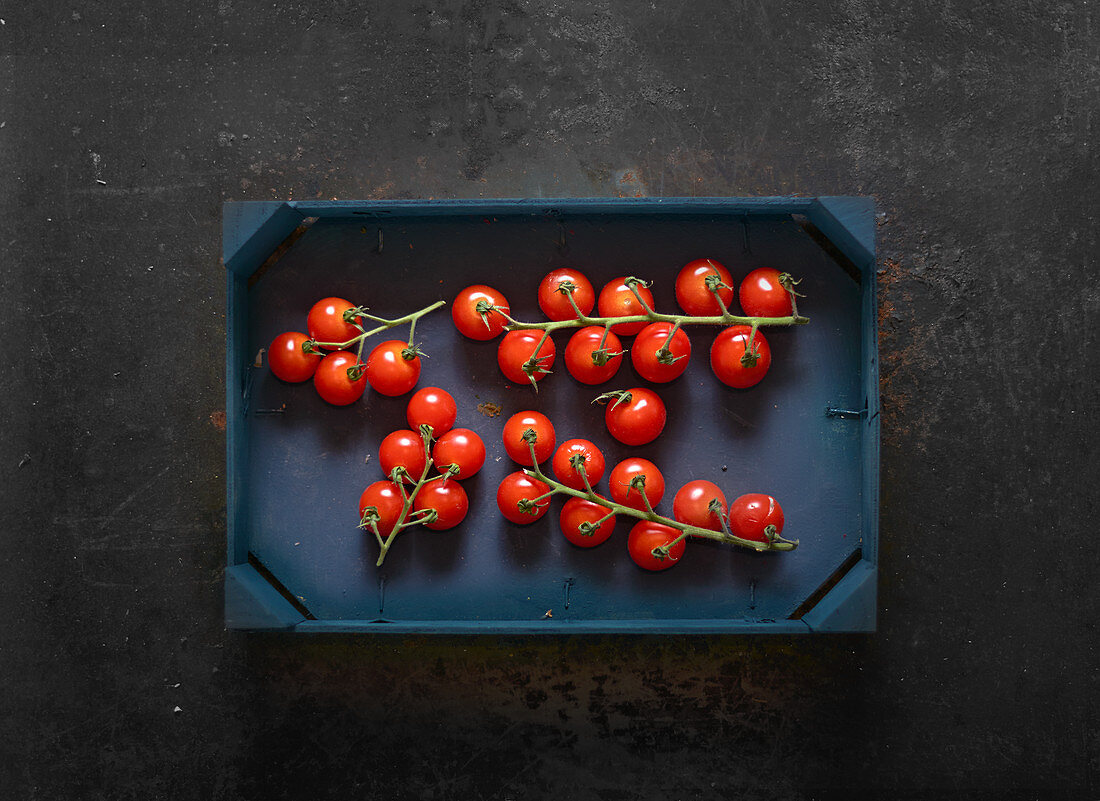 Kirschtomaten an Rispen in Holzspankiste