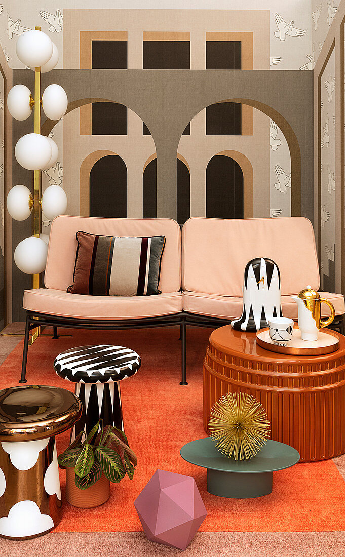Side tables in front of two-seater sofa against mural wallpaper with architectural motif