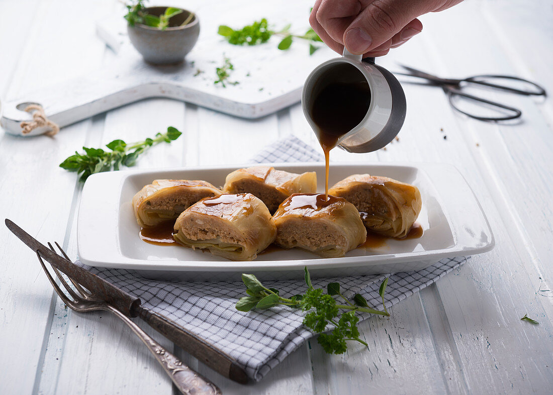 Gravy being poured over cabbage wraps filled with minced beans