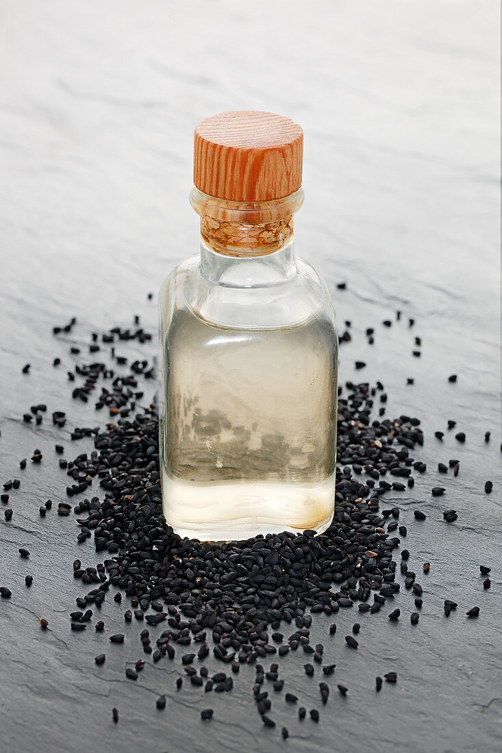 A bottle of sesame seed oil surrounded by black sesame seeds