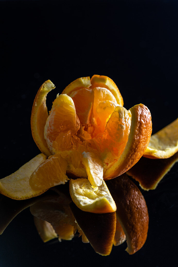 A peeled orange broken into segments against a black background