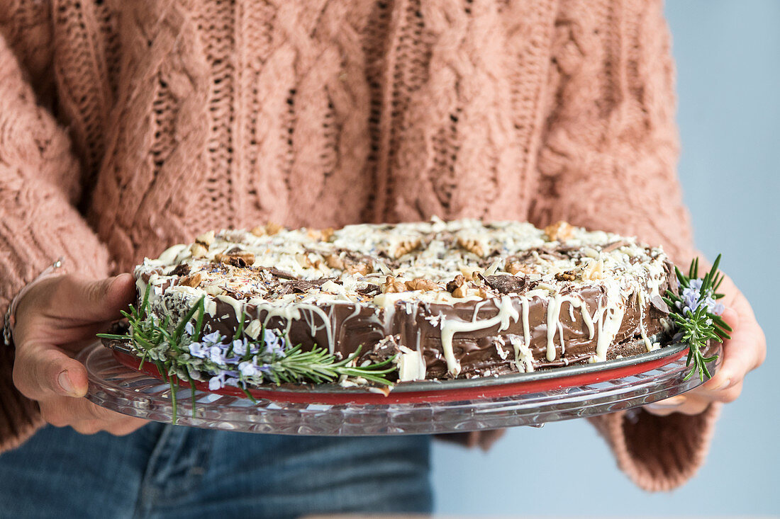 A woman holding a vegan chocolate cake decorated with white chocolate