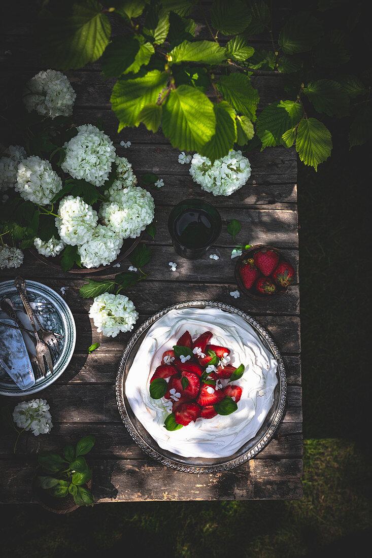 Pavlova mit Erdbeeren und Basilikum auf Tisch im Freien