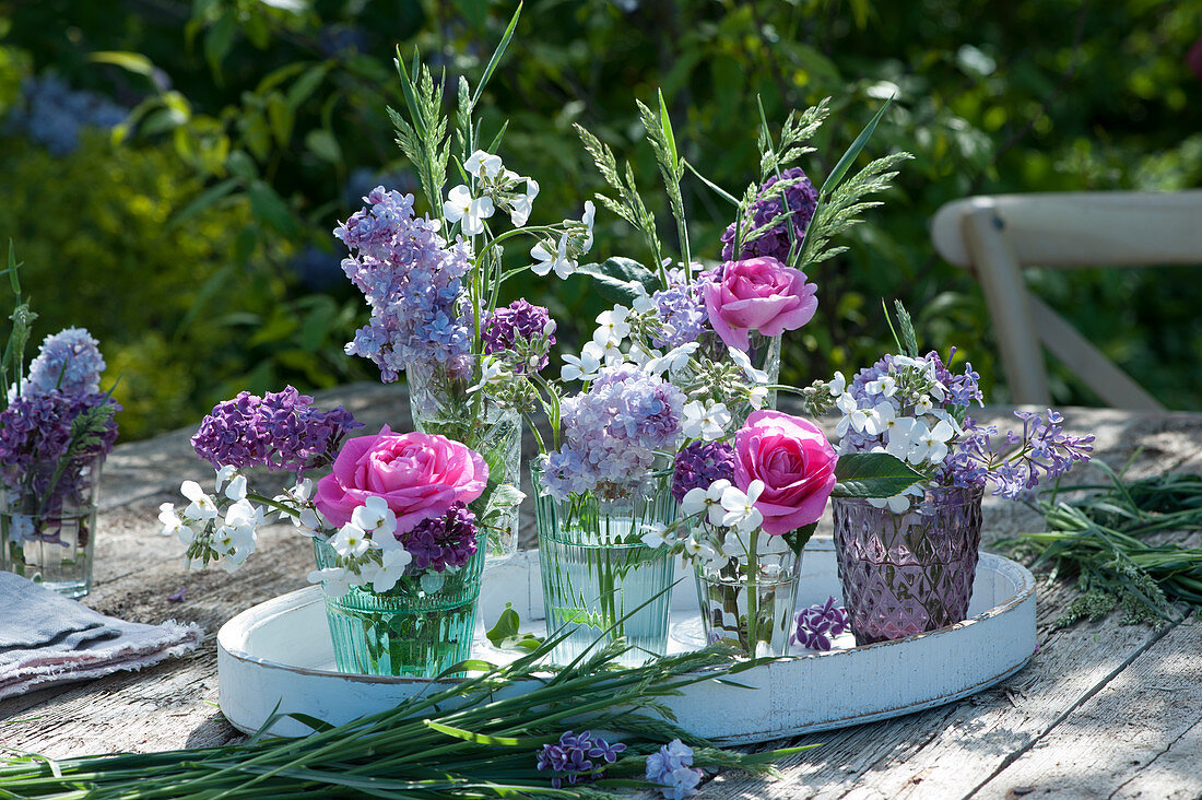 Small bouquets of roses, lilacs, night violes and grasses on a wooden tray