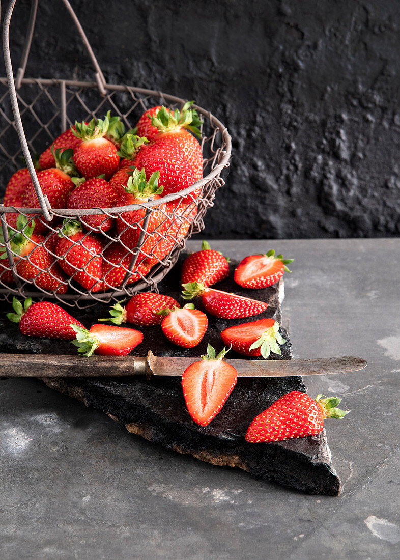 Frische Erdbeeren im Drahtkorb und halbiert auf Steinplatte