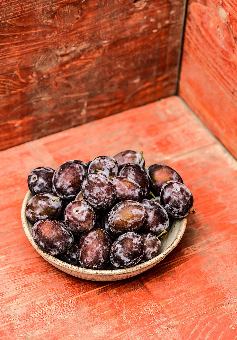 Several plums in a stone bowl on a red wooden plate