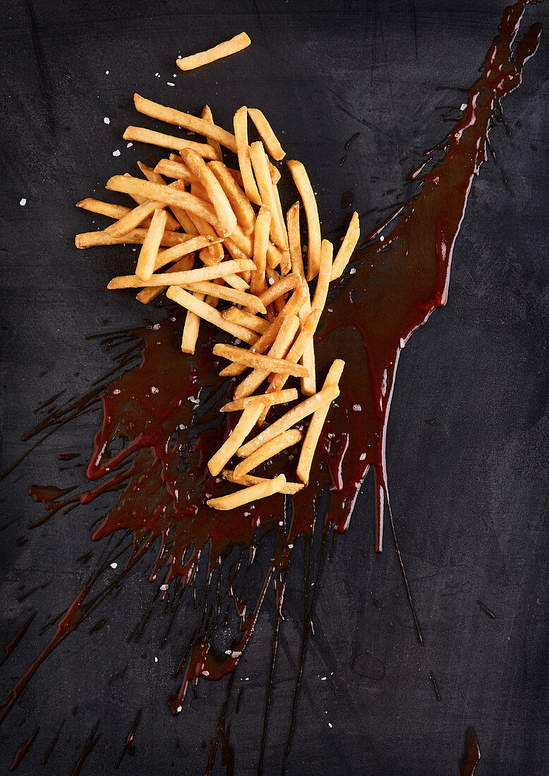 Grosser Klecks Ketchup mit Pommes frites und Salz auf schwarzem Untergrund