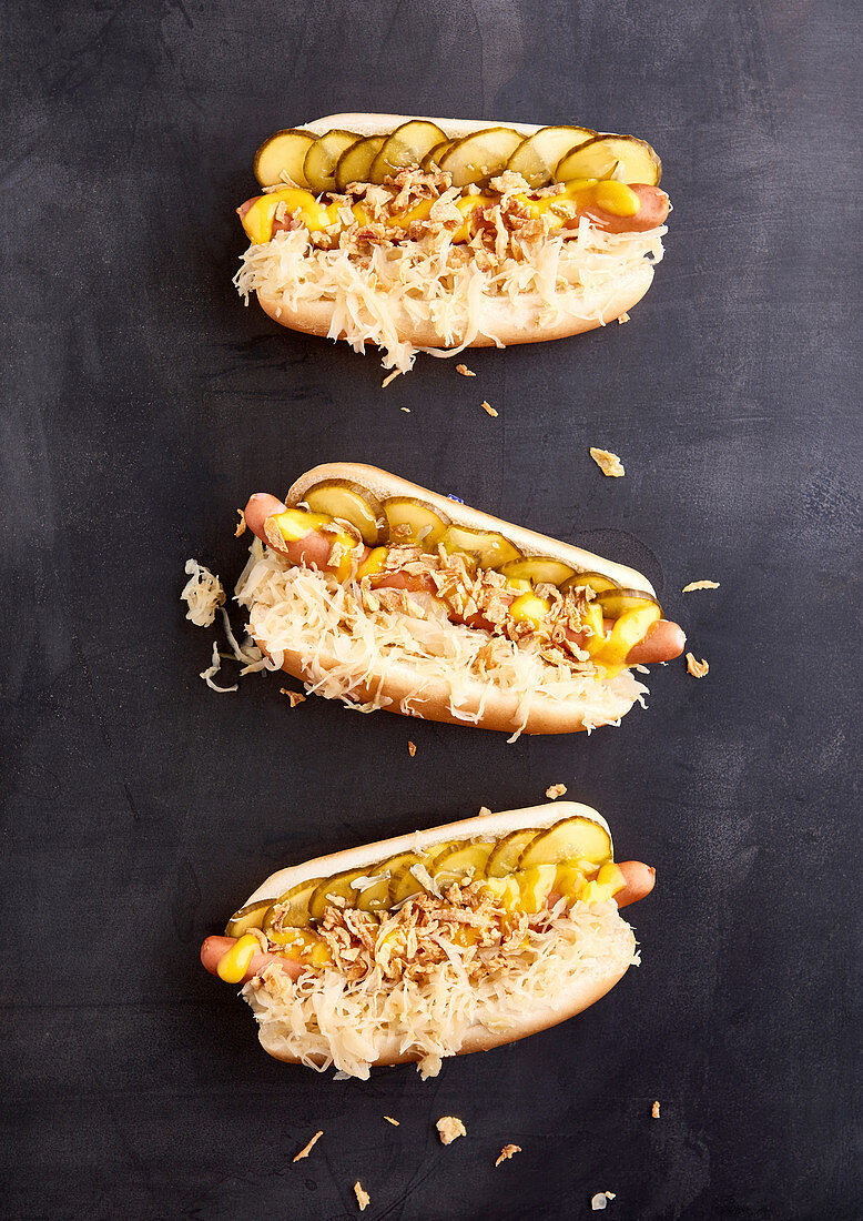 Drei Hotdogs mit Brühwürstchen, Sauerkraut, Gewürzgurken, Senf und Röstzwiebeln