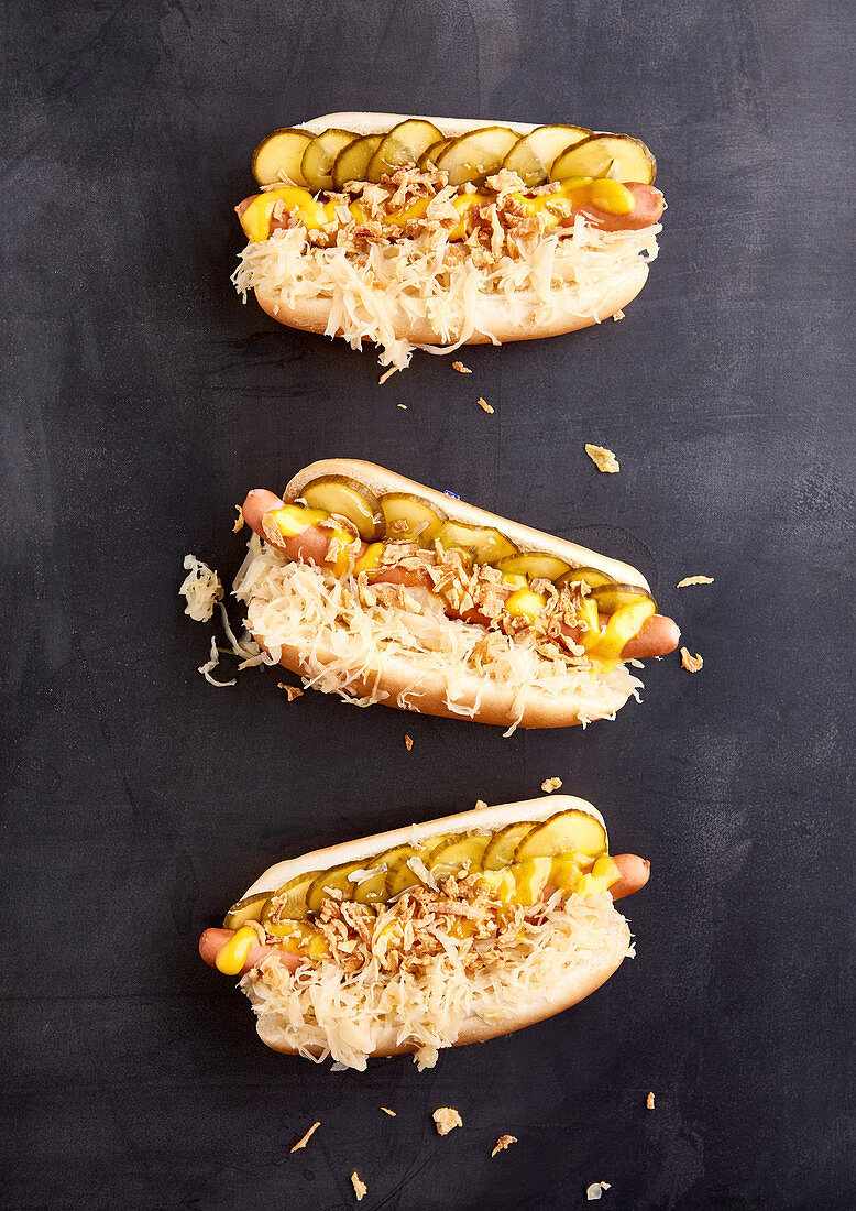 Three hot dogs with cooked sausages, sauerkraut, pickled cucumbers, mustard and roasted onions