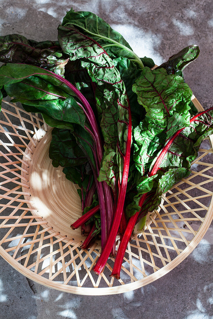 A wooden basket of rainbow swiss chard, sitting on an outdoor stone surface
