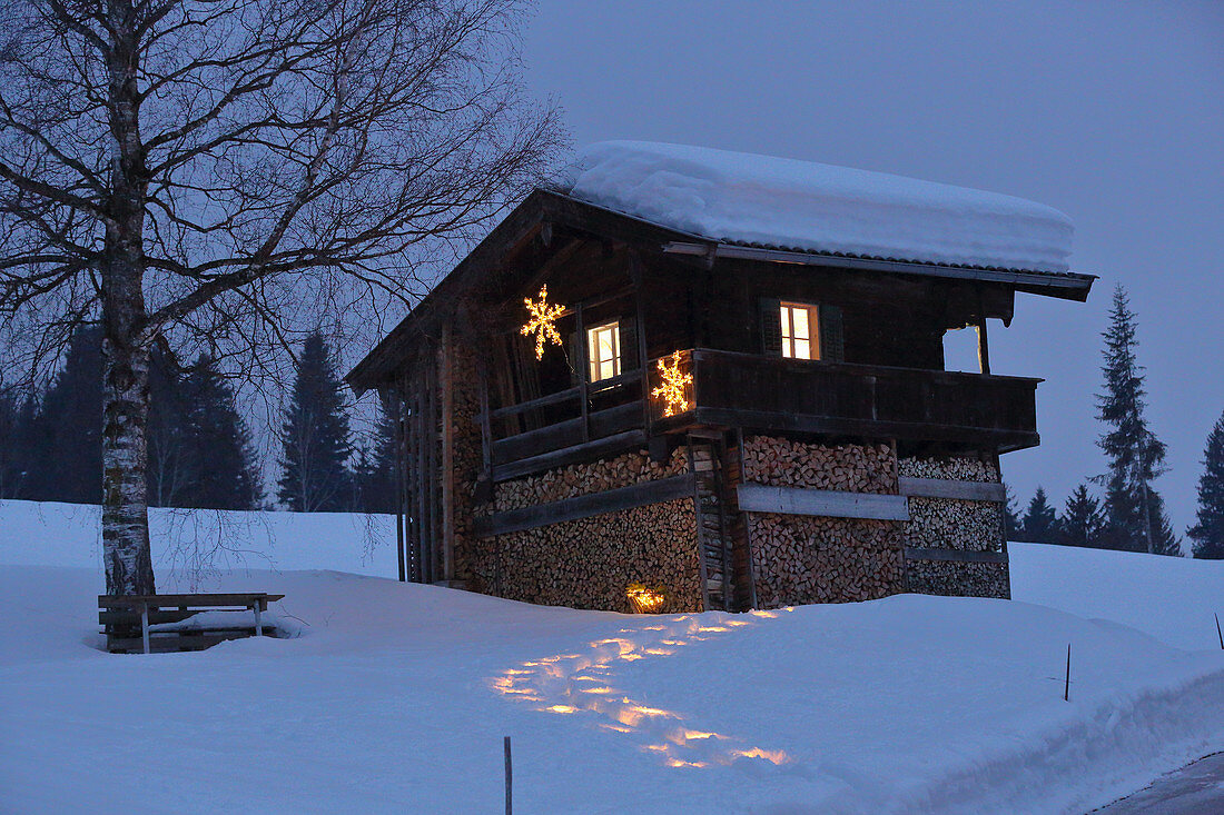 Illuminated, snowy path leading to Alpine cabin at twilight