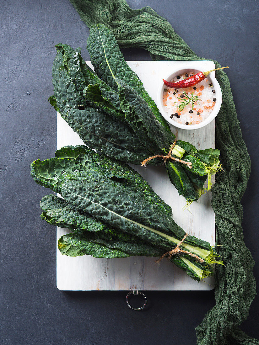 Raw black (Tuscan) kale on white chopping board with salt and spices.