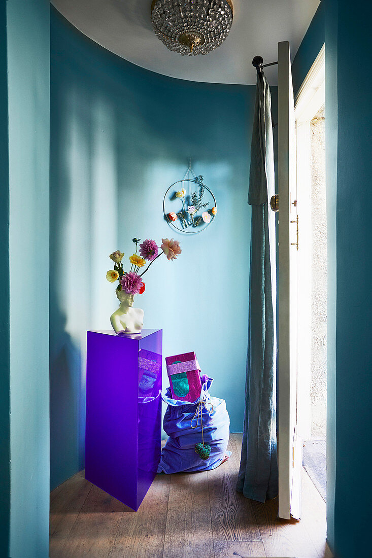 Büsten-Vase auf violettem Sockel vor blauer, geschwungener Wand