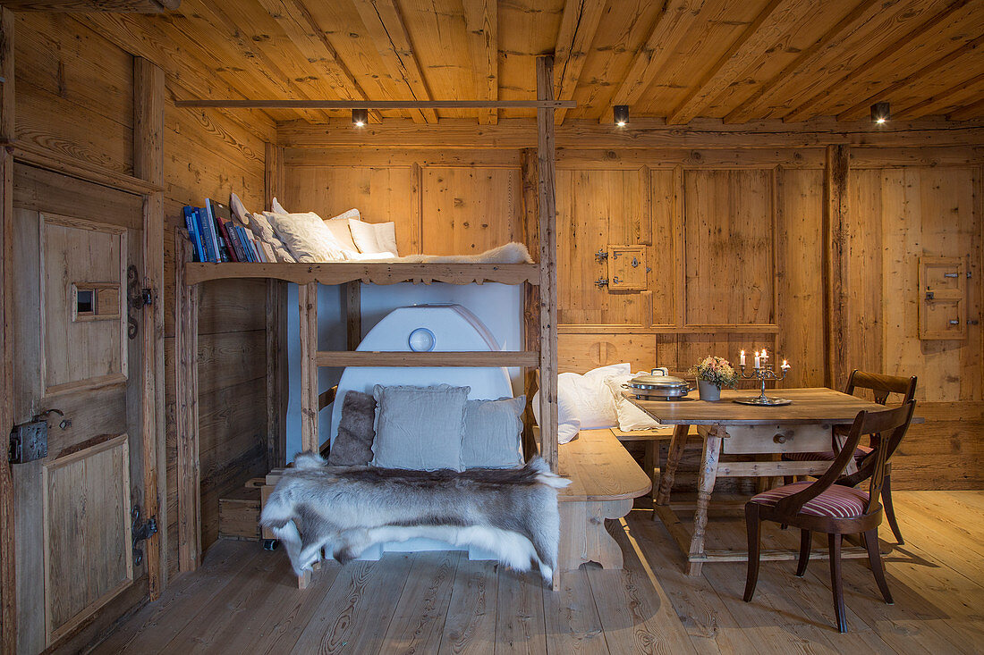 Loft bed above masonry stove and dining table in rustic farmhouse parlour