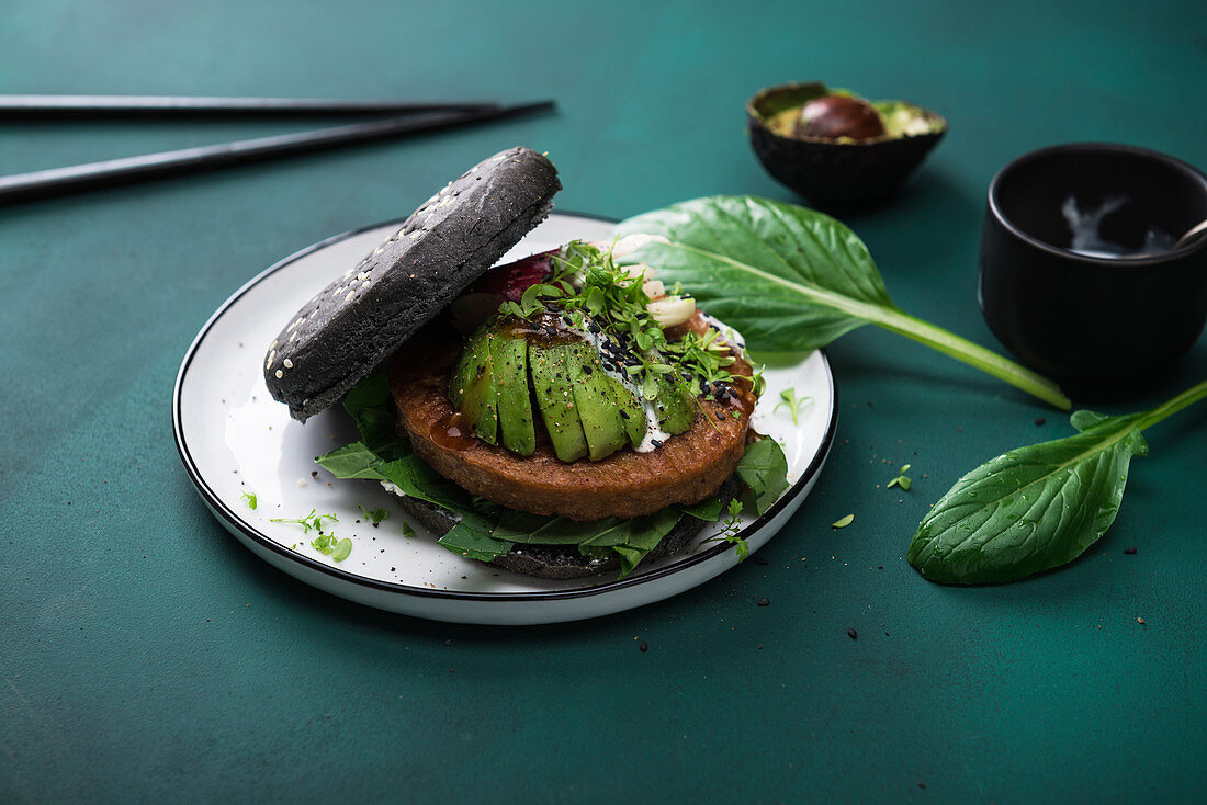 Soja-Weizenprotein-Bratling mit Avocado, Radieschen und zweierlei Saucen im schwarzen Burgerbrötchen