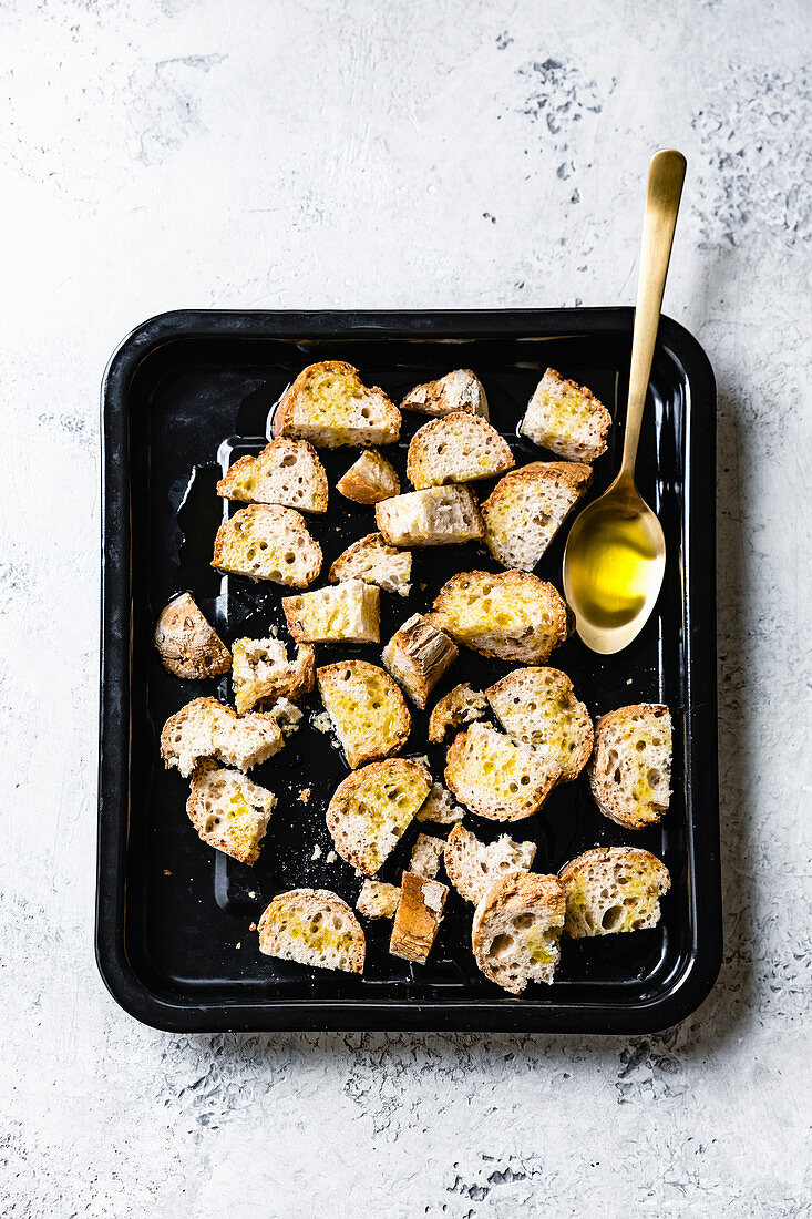 Mit Olivenöl beträufelte Brotstücke auf einem Backblech