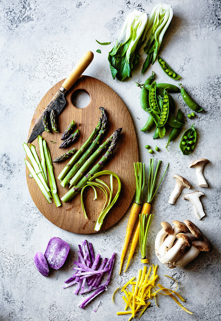 Sliced asparagus on a wooden cutting board with a selection of fresh colourful vegetables.