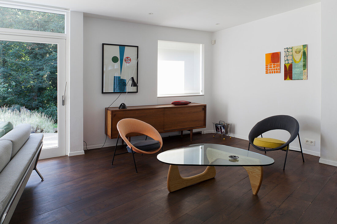 Glass-topped coffee table, two chairs and sideboard in retro interior