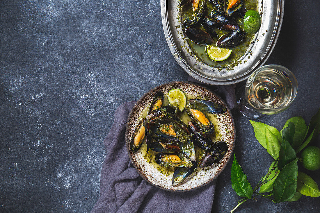 Mussels in green herb and white wine sauce with lemon on dark background.