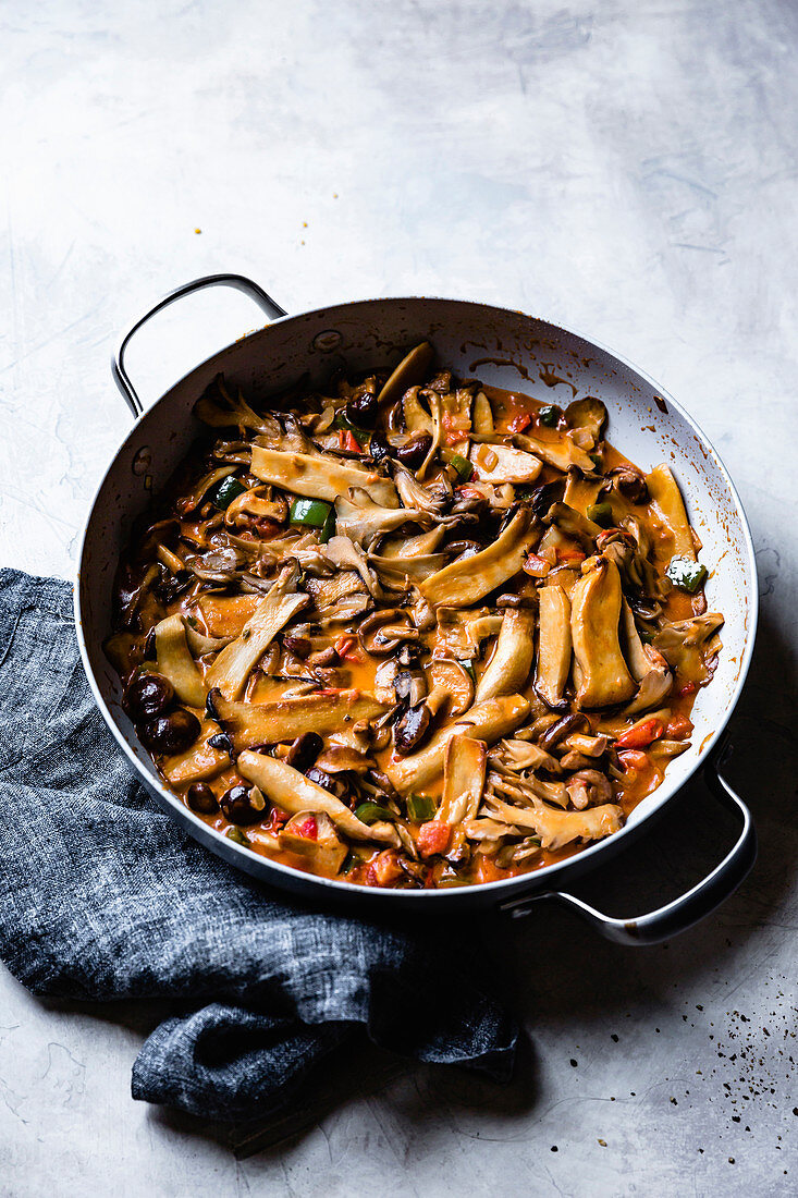 Sliced mushrooms and peppers sauteed in a pan.