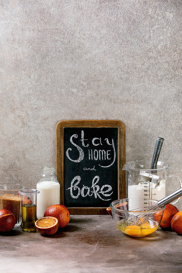 Kreidetafel mit Aufschrift 'Stay home and bake' zwischen Backzutaten