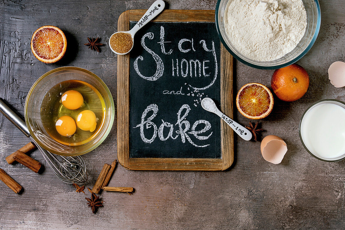 Ingredients for baking. Stay home quarantine isolation period concept. Vintage chalkboard with handwritten chalk lettering Stay home and bake. Grey texture background. Flat lay, space