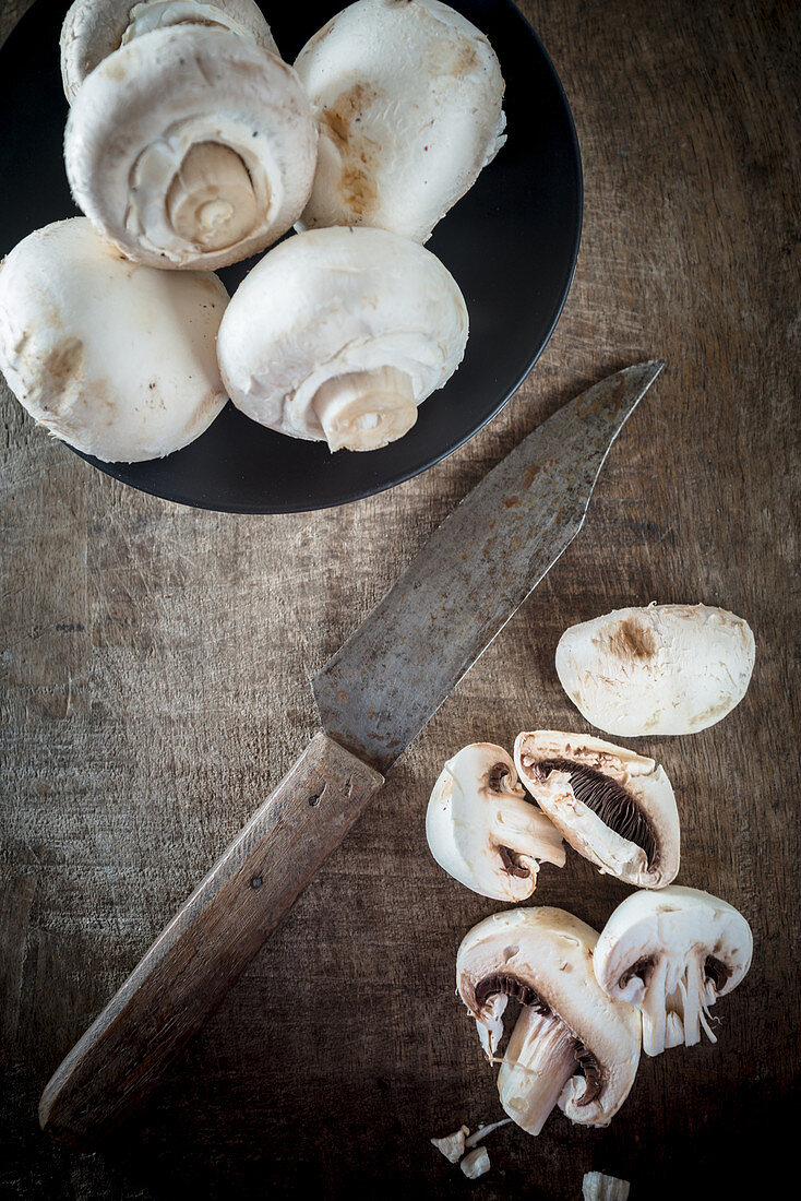 Button Mushrooms on a wooden board with a knife