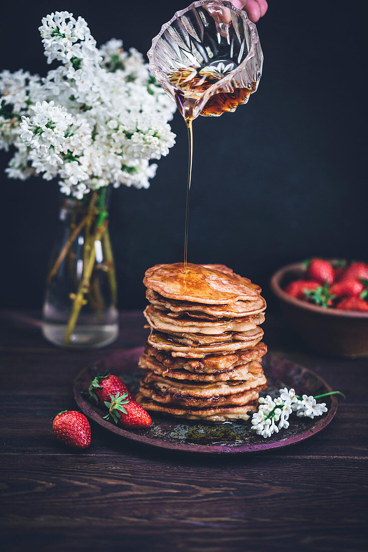 Pouring maple syrup on top of stack of pancakes