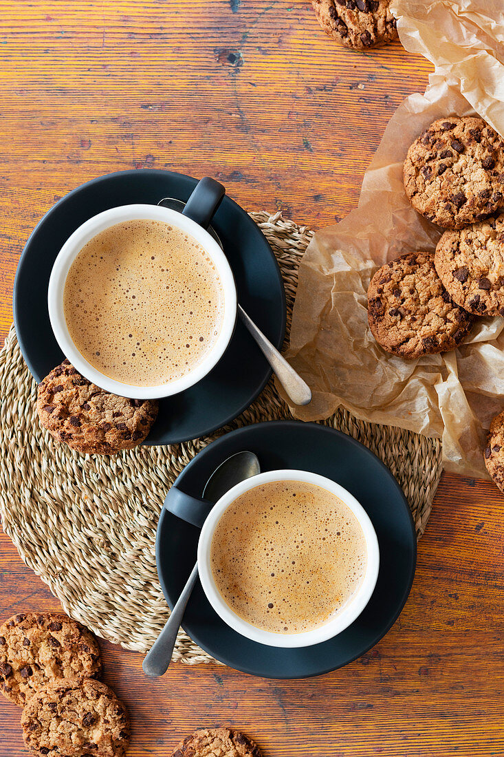 Cups of cappuccinno coffee with chocolate chip cookies on baking paper.