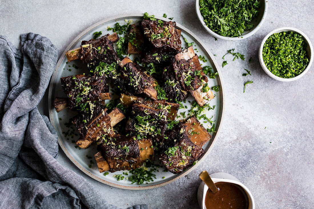 Roasted beef ribs with chopped parsley and chives on a plate.