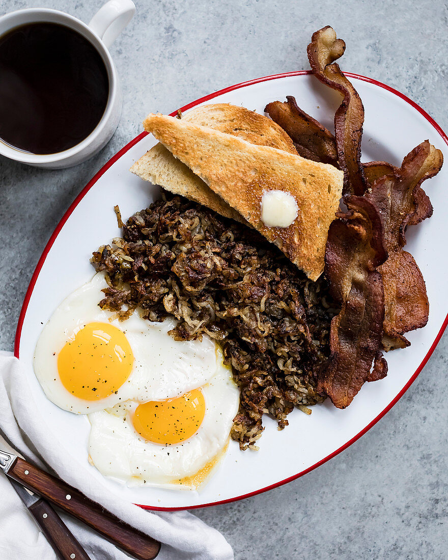 Fried eggs, onion and bacon with buttered toast on a plate.