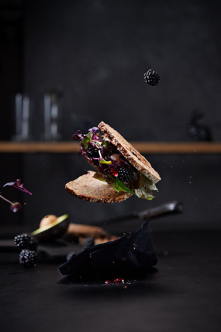 A floating sandwich with avocado, blackberries and salad