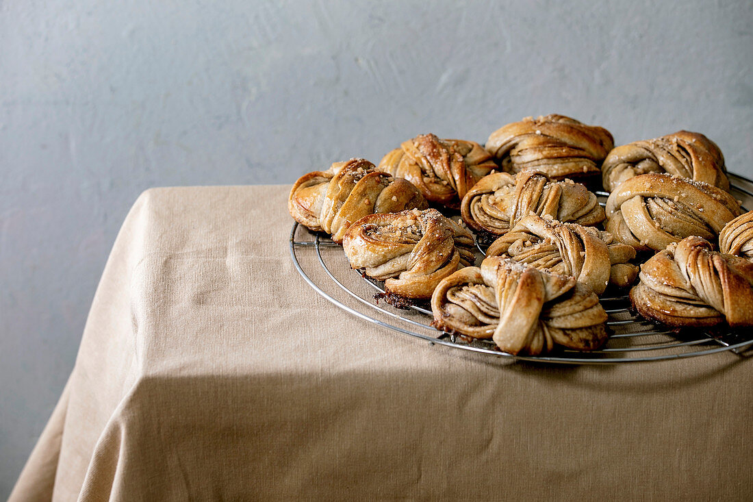 Traditional Swedish cardamom sweet buns Kanelbulle on cooling rack on beige linen table cloth.