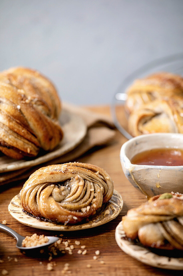 Traditional Swedish cardamom sweet buns Kanelbulle on plate, ingredients in ceramic bowl above on wooden table.