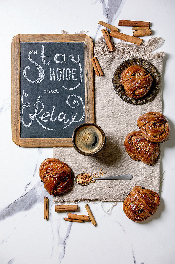 Traditional Swedish cinnamon sweet buns Kanelbulle on vintage tray, cup of coffee on linen cloth, chalkboard handwritten lettering Stay home and relax. White marble background, flat lay, space